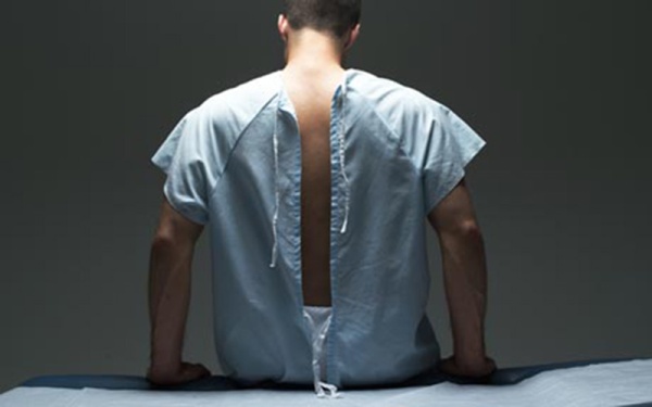 Man in hospital gown sitting on examination table, rear view